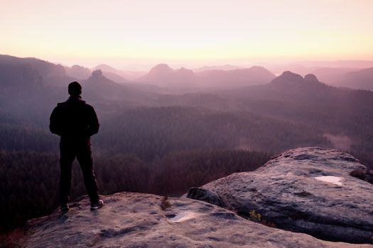 Tall man in black on cliff and watch to mountain sunrise.Silhouette in selfconfident pose.  Dark silhouette of rocks.