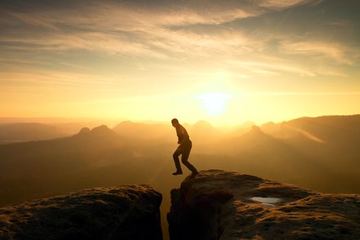 Young crazy man jump on mountain peak. Silhouette of jumping man and beautiful sunset sky. Vintage effect, lens defect.