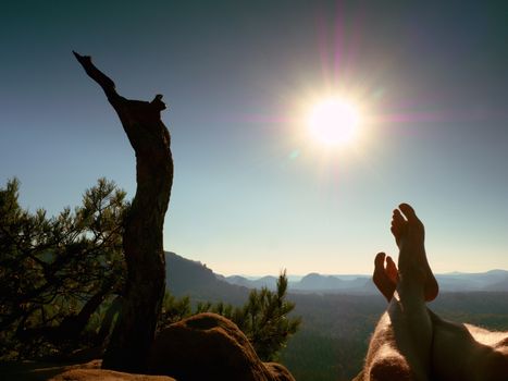 Naked male sweaty legs on peak of rock at broken pine tree. Hot windless summer day. Man take a rest on the treeking trip. Poor lighting effect.