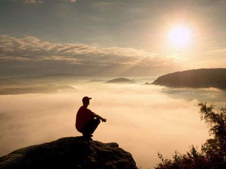 Man tourist  sit on rock empire. View point with heather and branches  above misty valley. Sunny daybreak in rocky mountains.