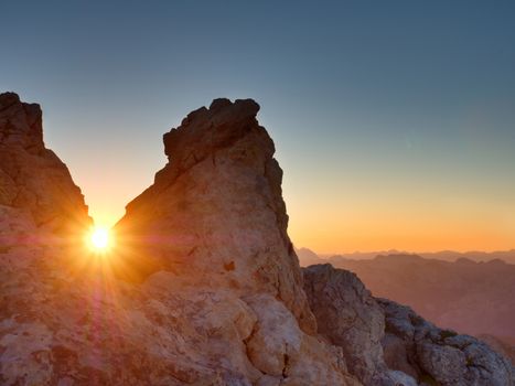 Lens flare light, strong effect. Morning sun between shar rocks,  Alpine  cliff above valley. Daybreak Sun at horizon. Mountains background