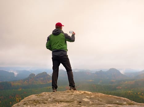 Man photography with phone of dreamy hilly landscape, spring orange pink misty sunrise in a beautiful valley of rocky mfountains.