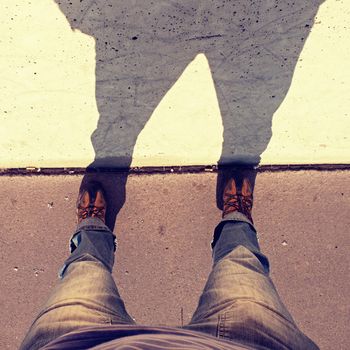 Man long legs stand on street at concrete wall with strong shadow. Silhouette of legs on the scratched wall. Crazy moment with camera on the empty street.