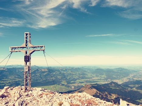 Praying cross raised at mountain summit in Alps. Sharp peak, daybreak Sun in sky. Steel crucifix in memory of victims of mountains. Vivid photo.
