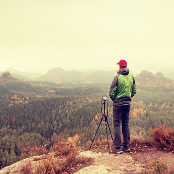 Photographer stay on cliff. Nature photographer takes photos with mirror camera on peak of rock. Dreamy fogy landscape