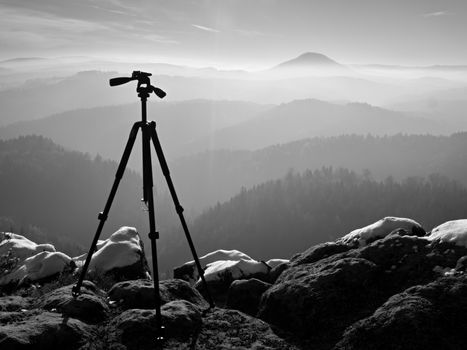 Professional  tripod without camera on snowy peak ready for photography. Snowy sandstone boulders,  first strong sun rays. 