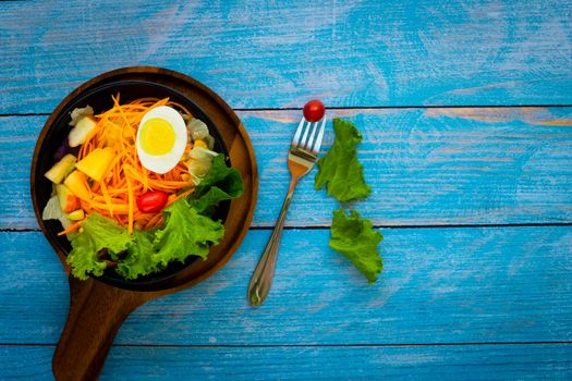 Good health and vegetarian concept, healthy vegetable salad of green fresh vegetable, carrot, corn, and fruit with milk and egg on plate on dark blue wood table background