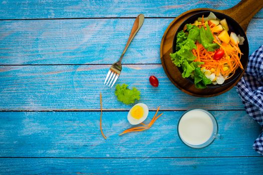 Good health and vegetarian concept, healthy vegetable salad of green fresh vegetable, carrot, corn, and fruit with milk and egg on plate on dark blue wood table background