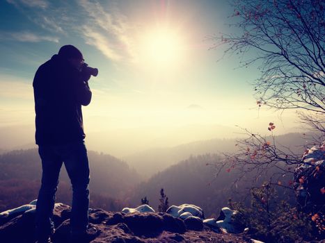Tall  man is taking photo by mirror camera on neck. Snowy rocky peak of mountain. Professional photographer takes photos with mirror camera on peak of snowy rock. 