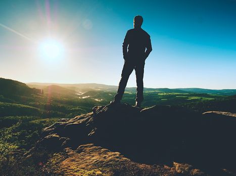 Man stands on the peak of sandstone rock  watching over valley to Sun. Beautiful moment the miracle of nature