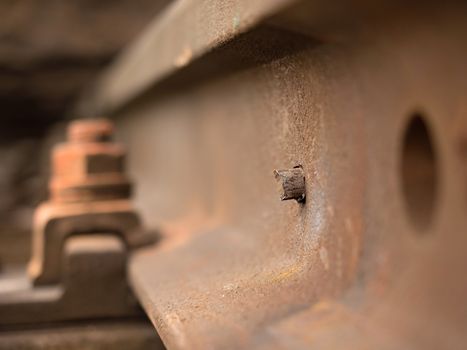 Detail of rusty screws and nut on old railroad track. Rotten wooden tie with rusty nuts and bolts. Damaged wooden railway sleeper. No train passed this railroad for a long time.
