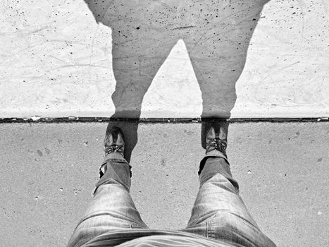 Man long legs stand on street at concrete wall with strong shadow. Silhouette of legs on the scratched wall. Crazy moment with camera on the empty street.