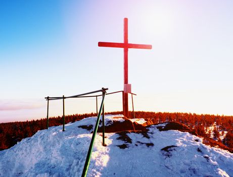 Modest wooden cross raised  on rocky mountain summit . Sharp snowy peak. Daybreak Sun in sky. Wooden unpretentious crucifix in memory of victims of mountains. Vivid photo.
