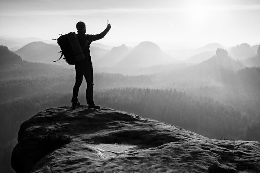 Strong man hiker taking photo with smart phone at mountain peak. Marvelous daybreak.
