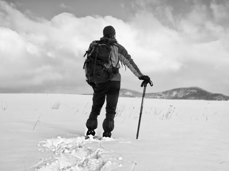 Hiker with backpack snowshoeing  in deep drift. Man with snowshoes walk in hill. Hiker in green gray winter jacket and black trekking trousers snowshoeing in powder snow.