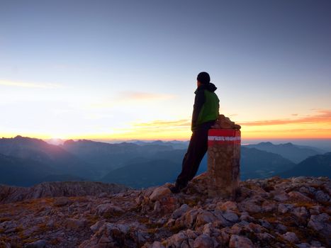 Tired hiker sit on border stone on Alpine mountain. Austria Germany border. Daybreak horizon above blue foggy valley. Mountains increased from humidity