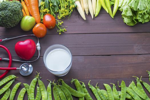 Healthy food, vegetables organic on wooden background with glass of milk and stethoscopes with red heart, strong body concept.