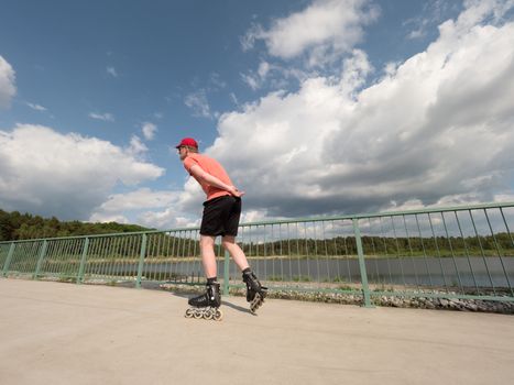 Roller skater in action. Man ride in inline skates ride along promenade handrail, blue sky in background. Low angle view