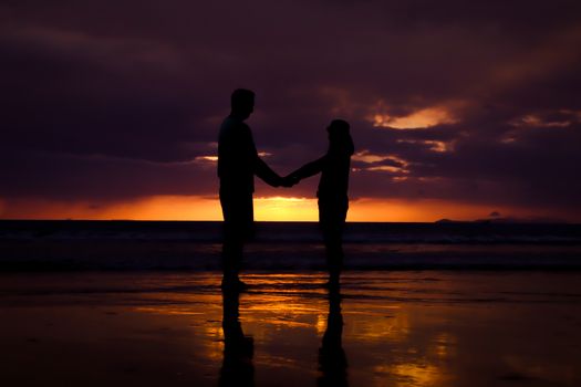 Silhouette of couple hold each other hand and Happy Young Couple love on the beach at sunset time