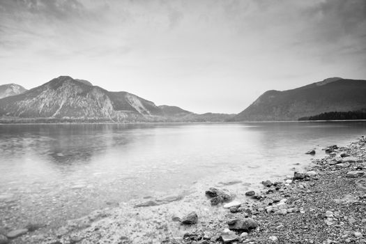 Cloudy sunset at mountain lake. Stony beach and dark mountains  in water mirror. Evening after heavy rainy day.  Poor lighting conditions.