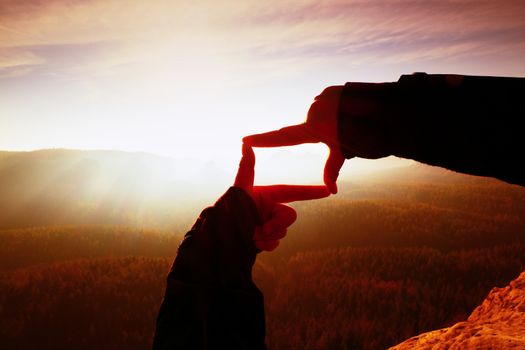 Close up hands making frame gesture. Orange misty valley bellow. Sunny spring daybreak in mountains. Red vintage style.