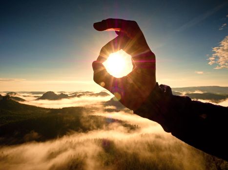 Man hand touch Sun. Misty daybreak in a beautiful hills. Peaks of hills are sticking out from foggy background, the fog is red and orange due to Sun rays. Lens defects.