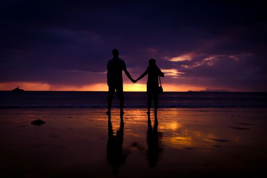 Silhouette of couple hold each other hand and Happy Young Couple love on the beach at sunset time