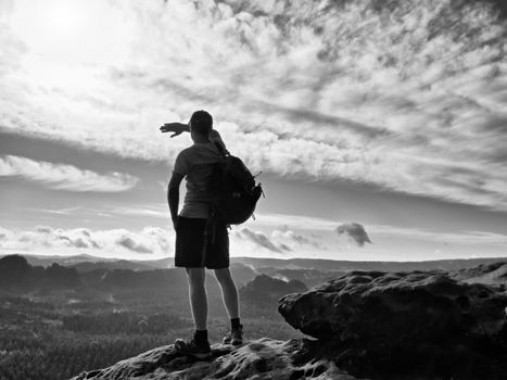 Man shadowing eyes. Alone tourist with red  baseball cap sporty backpack stand on cliff edge and watching into deep valley bellow. Spring weather. Vintage Style Toned effect