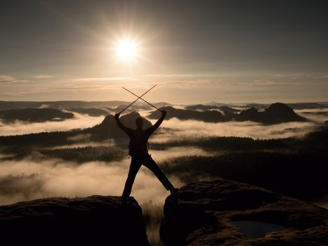 Hiker on peak. Tourist with bag in target with trekking poles in hand raised in air. Marvelous daybreak in fogy mountains