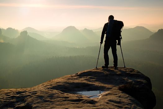 Tourist with leg in immobilizer. Hiker silhouette with medicine crutch on mountain peak. Deep misty valley bellow silhouette of man with hand in air. Spring daybreak