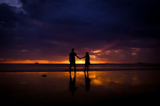 Silhouette of couple hold each other hand and Happy Young Couple love on the beach at sunset time