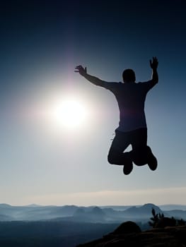 Young crazy man is jumping on mountain peak. Silhouette of jumping man and beautiful sunset sky. Element of design. Vintage effect.