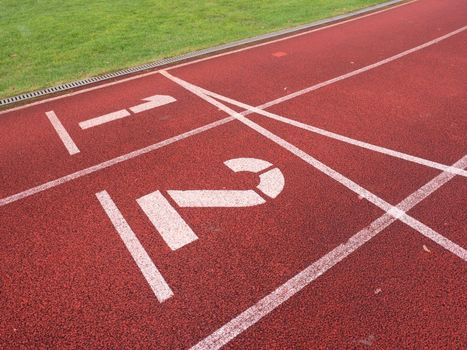 White track number on red rubber racetrack, texture of running racetracks in small stadium. Number one and number two. Outdoor excercise. 