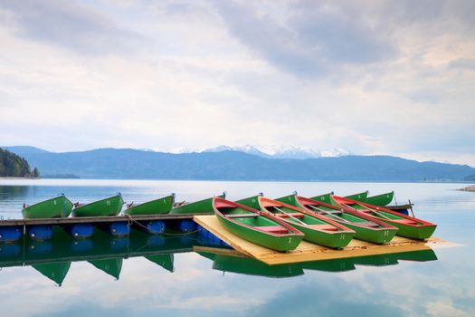 Blue Alps lake with Rental rowing boats in marina. Wharf for trip ships.