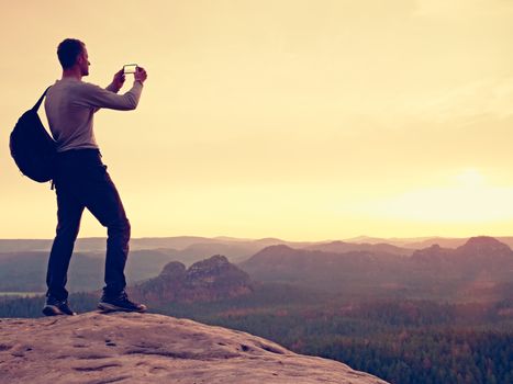 Sportsman take selfie photo with phone at mountain peak. Man with phone in hand. Misty mountains at horizon. Marvelous daybreak.