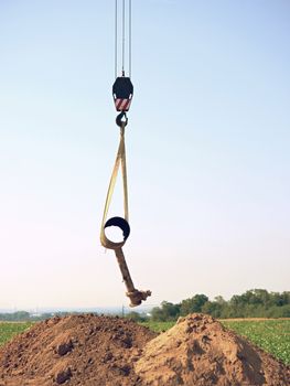 Hanging old tube on crane rope. Clear blue sky in background