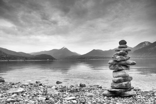 Balanced stone pyramide on shore of blue water of mountain lake. Blue mountains in water level mirror