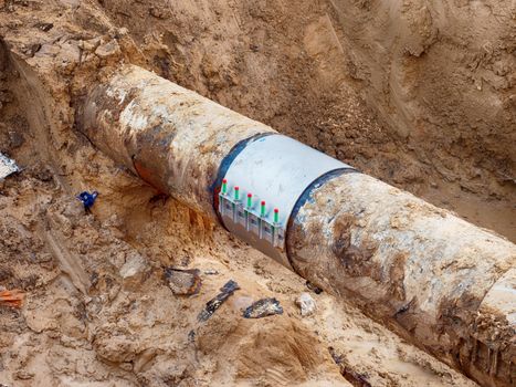 Excavation pit. Old drink water pipe with  stainless repairing sleeve members. Finished repaired piping waiting for covering by clay. Asphalt isolation. 