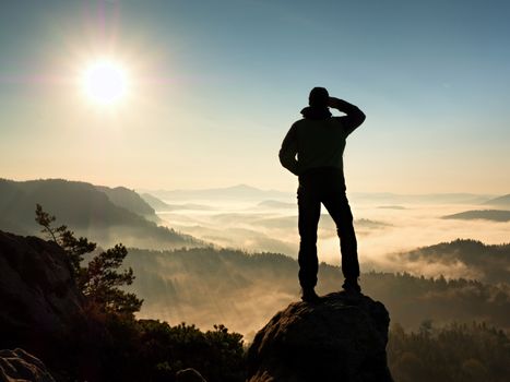 Man silhouette stay on sharp rock peak. Satisfy hiker enjoy view. Tall man on rocky cliff watching down to landscape. Vivid and strong vignetting effect.