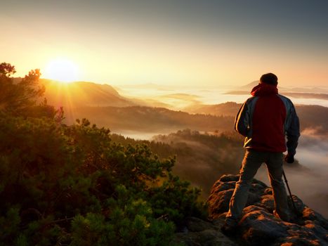 Happy photo enthusiast  enjoy  photography of  fall daybreak in nature on cliff on rock. Dreamy fogy landscape, misty sunrise in a beautiful valley below