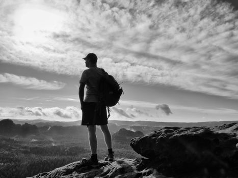 Alone tourist with red  baseball cap sporty backpack stand on cliff edge and watching into deep valley bellow. Spring weather. Vintage Style Toned effect