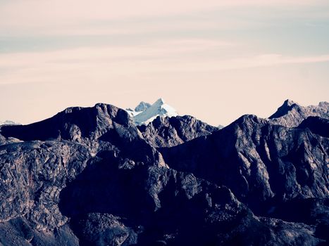 Far rocky peak of Alps mountain in sunny winter day. Rock under fresh powder snow. 