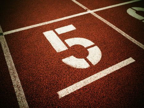 Number five. Big white track number on red rubber racetrack. Gentle textured running racetracks in small athletic stadium.