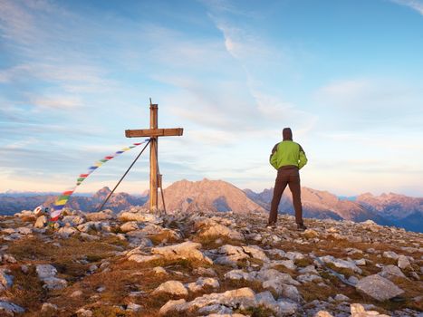 Man walk along the wooden cross at a mountain peak built to Alps victiims. Cross on top of a mountain peak as typical in the Alps.  Rocky view point above misty Alpins valley. 