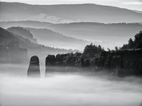 Fantastic sunrise on the top of the rocky mountain with the view into misty valley. Black and white photo