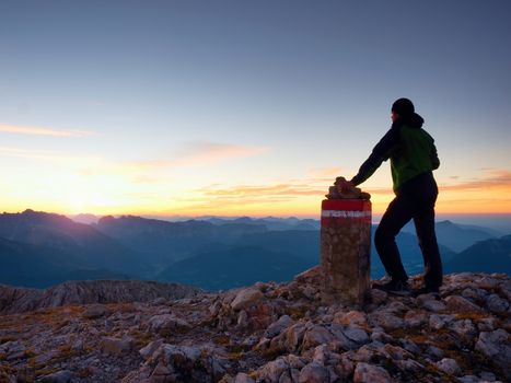 Alone hiker against of Austria Germany border stone on Alpine mountain. Daybreak horizon above blue foggy valley. Mountains increased from humidity