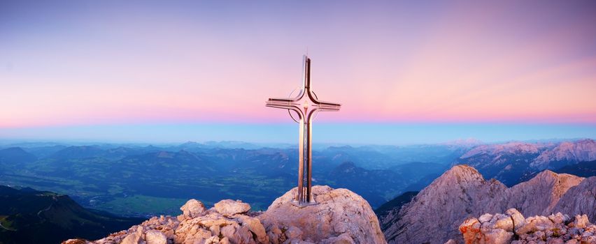 Hoher Goell autumn daybreak panorama. Iron cross at mountain top in Alp at Austria Germany border.  View to Tennen Range and Dachstein range, Berchtesgaden Alps.