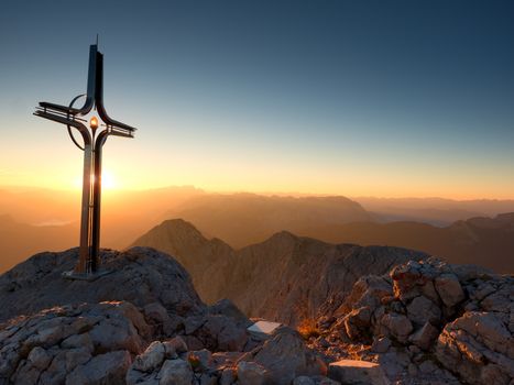 Cross raised  at mountain summit  in Alps. Sharp peak, daybreak Sun in sky. Steel crucifix in memory of victims of mountains. Vivid photo.