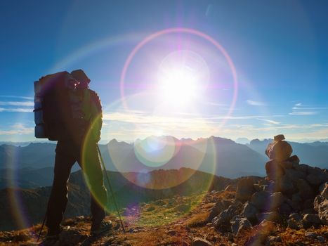 Lens flare light, strong defect. Man hiker with rucksack walk  on rocky peak. Tourist  walking over rocky summit to Sun. Beautiful moment the miracle of nature.