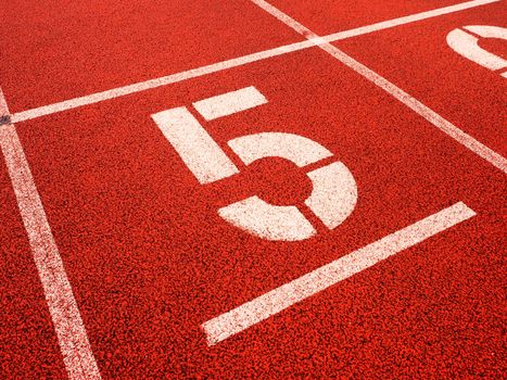 Number five. Big white track number on red rubber racetrack. Gentle textured running racetracks in small athletic stadium.